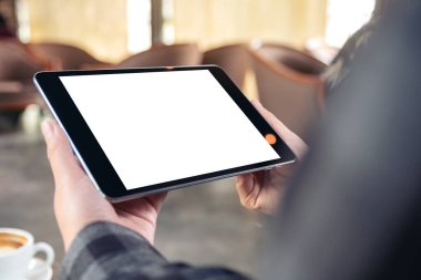 Boş beyaz masaüstü ekran ve kafede kahve fincanı olan siyah tablet tableti tutan ve kullanan ellerin görüntüsünü taklit et