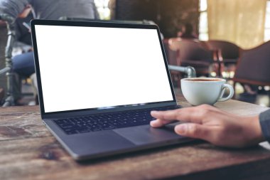 Kafedeki ahşap masada kahve fincanı ve boş beyaz masaüstü ekranı olan bir bilgisayarın dokunmatik ve kullanışlı el resmi.