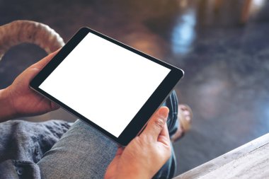 Kafede otururken elinde boş beyaz ekranlı siyah tablet tutan bir kadının görüntüsü.