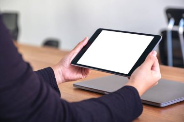 Ofisteki ahşap masadaki defter ile birlikte boş beyaz masaüstü ekranı olan siyah tablet bilgisayarın el ele tutuşunu ve kullanımını görüntüle