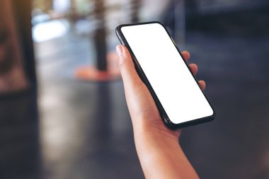 Kafede boş beyaz masaüstü ekran ile siyah cep telefonu tutan bir elin görüntüsü