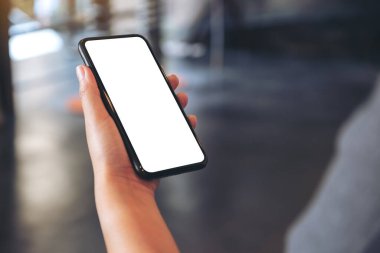 Kafede boş beyaz masaüstü ekran ile siyah cep telefonu tutan bir elin görüntüsü