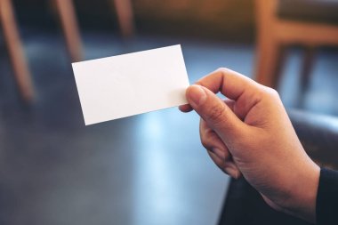 Arkaplanı bulanık, beyaz, boş bir kartvizit tutan bir el.