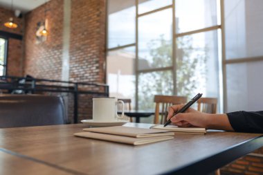 Kafe 'de kahve fincanı ile boş bir deftere el yazısının yakın plan resmi.