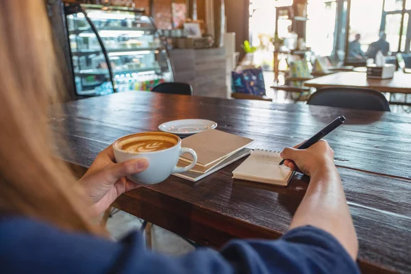 카페에 탁자에 공책에 쓰면서 뜨거운 커피를 마시는 여자의 모습을 클로즈업 — 스톡 사진
