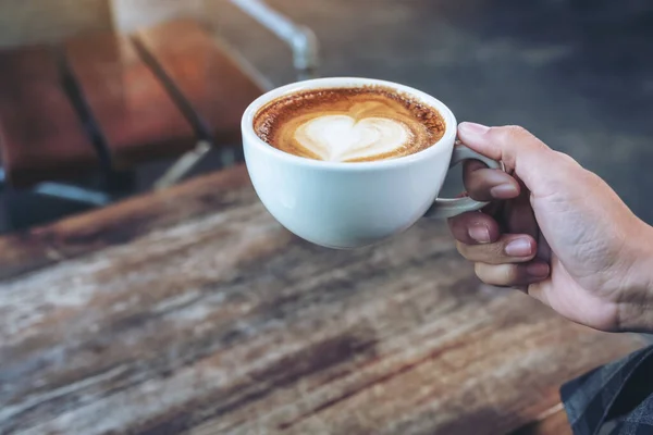 店内の木のテーブルの上に熱いコーヒーの青いカップを持っている手のクローズアップイメージ — ストック写真