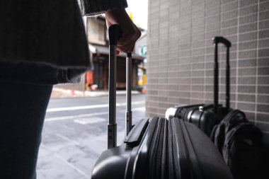 Siyah bavulu tutan ve sürükleyen bir kadının yakın plan görüntüsü.