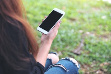 Yeşil bahçede otururken elinde boş siyah masaüstü ekran olan beyaz cep telefonu tutan kadının görüntüsü