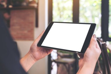 Kafedeki boş masaüstü ekranlı siyah tableti tutan kadınların ellerinin görüntüsü.