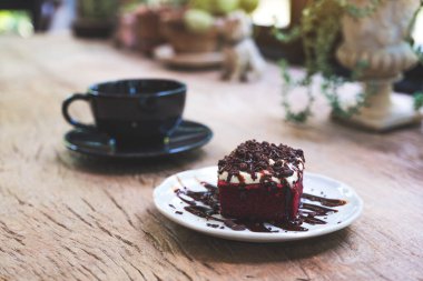 Kafedeki ahşap masada kahve fincanı olan kırmızı kadife bir kek.