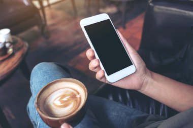 Kafede kahve içerken ellerinin beyaz cep telefonu ve boş siyah masaüstü ekran görüntüsü.