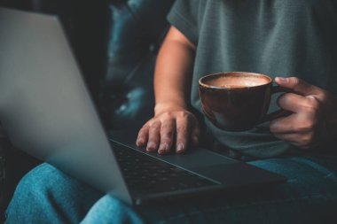 Kahve içerken dizüstü bilgisayarda çalışan ve daktilo kullanan bir kadının yakın plan görüntüsü.