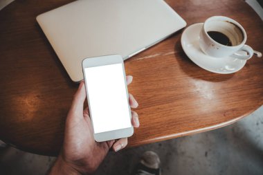 Masada kahve fincanı ve dizüstü bilgisayarı olan, boş masaüstü ekranlı beyaz cep telefonlu el kamerası görüntüsü