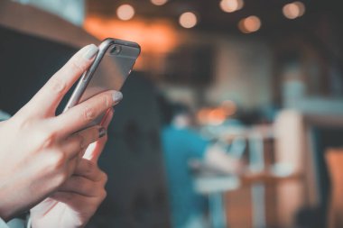 Kafede arka planı bulanık akıllı bir telefonu kullanan ve ona bakan bir kadının ellerinin yakın plan görüntüsü.