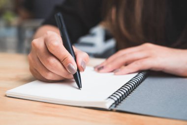 Tahta masaya beyaz boş bir defter yazan bir kadının yakın plan görüntüsü. 