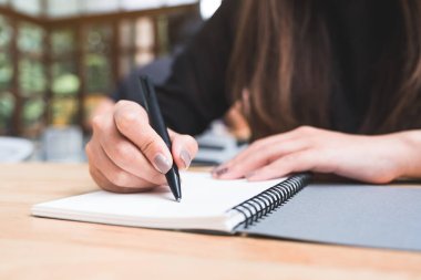 Tahta masaya beyaz boş bir defter yazan bir kadının yakın plan görüntüsü. 