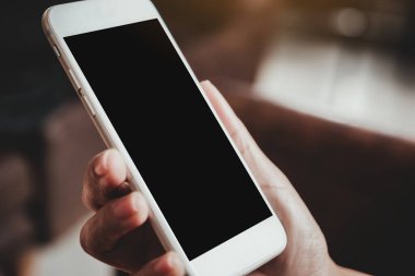 Boş siyah masaüstü ekranı ve bulanık arkaplanı olan beyaz cep telefonunu tutan bir elin görüntüsü