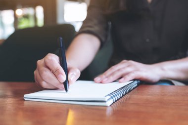 Tahta masaya beyaz boş bir defter yazan bir kadının yakın plan görüntüsü. 