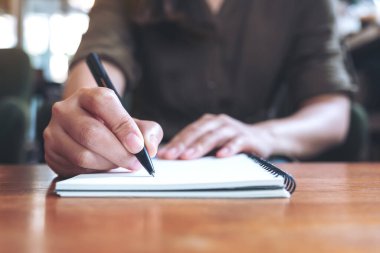 Tahta masaya beyaz boş bir defter yazan bir kadının yakın plan görüntüsü. 