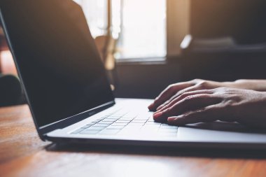 Tahta masadaki dizüstü bilgisayarın klavyesini kullanan ve yazan ellerin yakın plan resmi