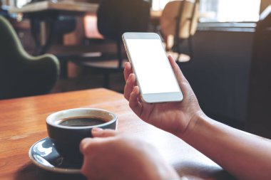 Modern kafede kahve içerken beyaz cep telefonunu boş ekran ile tutan ellerin görüntüsü.