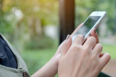 Yeşil doğalı akıllı bir telefonu tutan, kullanan ve dokunan bir kadının yakın plan görüntüsü.