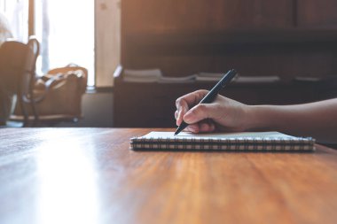 Tahta masaya beyaz boş bir defter yazan bir elin yakın plan resmi. 