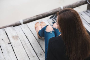 Asyalı bir kadının nehir kıyısındaki eski bir ahşap iskelede tek başına oturmasının en üst görüntüsü. 