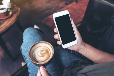 Üst görüntüde, kafede kahve içerken beyaz cep telefonu ve boş siyah masaüstü ekran görüntüsü var.