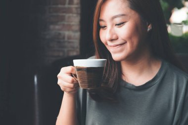 Asyalı bir kadının sıcak kahveyi tutarken ve içerken klasik kafede iyi hissettiği yakın plan görüntüsü.