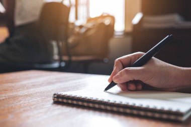 Tahta masaya beyaz boş bir defter yazan bir elin yakın plan resmi. 