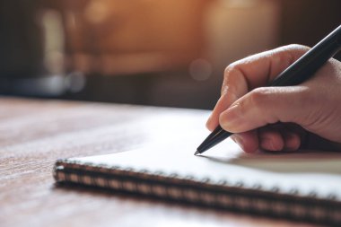 Tahta masaya beyaz boş bir defter yazan bir elin yakın plan resmi. 