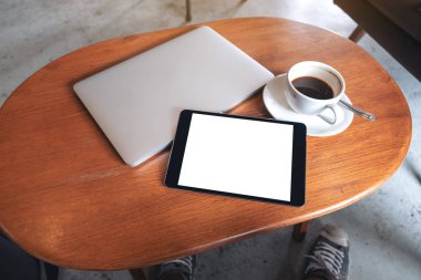 Boş masaüstü beyaz ekranlı, dizüstü bilgisayarlı ve ahşap masada kahve fincanı olan siyah bir tabletin görüntüsü