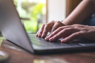 Tahta masadaki dizüstü bilgisayarın klavyesini kullanan ve yazan ellerin yakın plan resmi