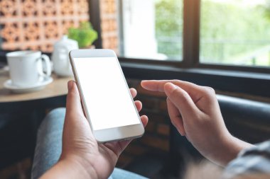 Modern kafede kahve fincanı olan beyaz cep telefonlu bir kadının el ele tutuşup işaret ettiği resim.