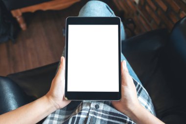 Üst görünümde çapraz bacaklı oturan ve elinde boş beyaz masaüstü ekranlı siyah tablet bilgisayar tutan bir kadının görüntüsü 
