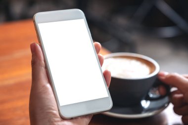Modern kafede kahve içerken beyaz cep telefonunu boş ekran ile tutan ellerin görüntüsü.