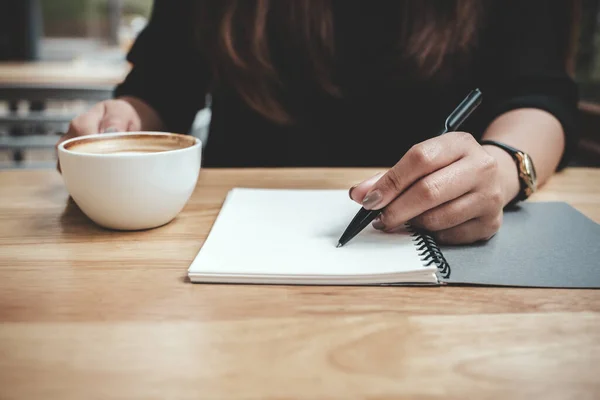 Imagem Perto Mão Uma Mulher Escrevendo Caderno Branco Enquanto Bebe — Fotografia de Stock