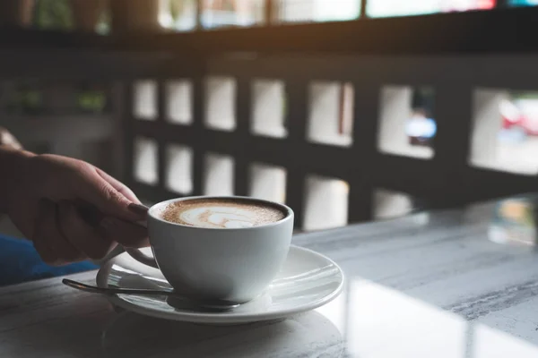 女性の手が熱いコーヒーを持っているイメージを閉じますハートラテアートとテーブルの上にカフェで — ストック写真