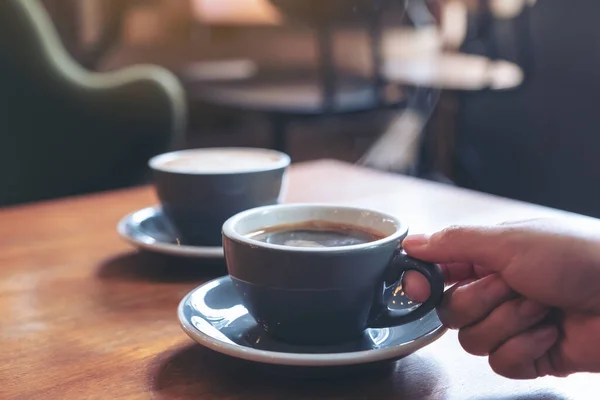 店内のテーブルに煙が立ち並ぶ熱いコーヒーの青いカップを持った手のイメージ — ストック写真