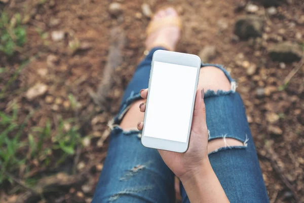 Üst görünümde, açık havada otururken elinde boş masaüstü ekran olan beyaz cep telefonu tutan kadının görüntüsü