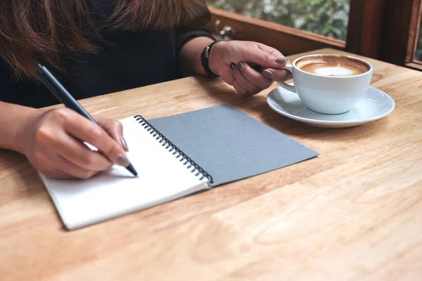 Imagem Perto Mão Uma Mulher Escrevendo Caderno Branco Enquanto Bebe — Fotografia de Stock