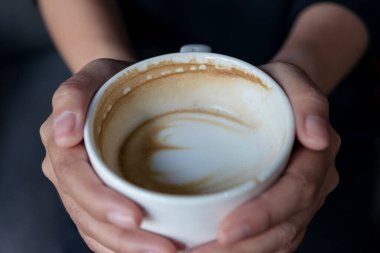 Bir kadının ellerinin beyaz bir fincan sıcak kahve tutarken görüntüsü. 