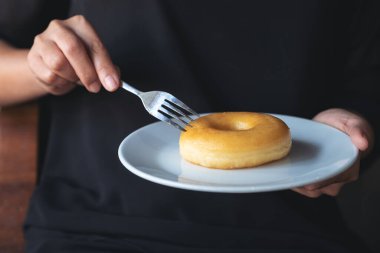 Bir kadının elleri bir parça çöreği beyaz bir tabakta tutuyor ve kesiyor.