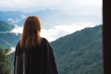 Sisli bir günde tek başına duran ve dağlara bakan bir kadın. Mavi gökyüzü arka planında sabah.