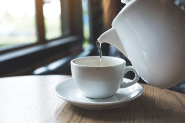 Çaydanlığı tutan ve beyaz bir fincana çay döken bir el.