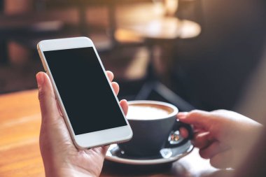 Modern kafede kahve içerken beyaz cep telefonunu boş ekran ile tutan ellerin görüntüsü.
