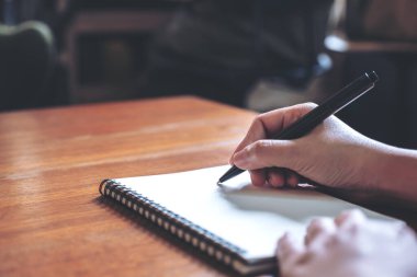 Tahta masaya beyaz boş bir defter yazan bir elin yakın plan resmi.