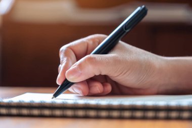 Tahta masaya beyaz boş bir defter yazan bir elin yakın plan resmi.