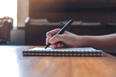 Tahta masaya beyaz boş bir defter yazan bir elin yakın plan resmi. 